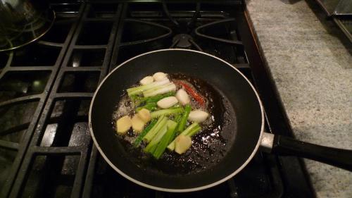 Place chopped green onions (2) and 5 cloves of garlic. three pieces of ginger, and a stalk of red pepper into hot oil